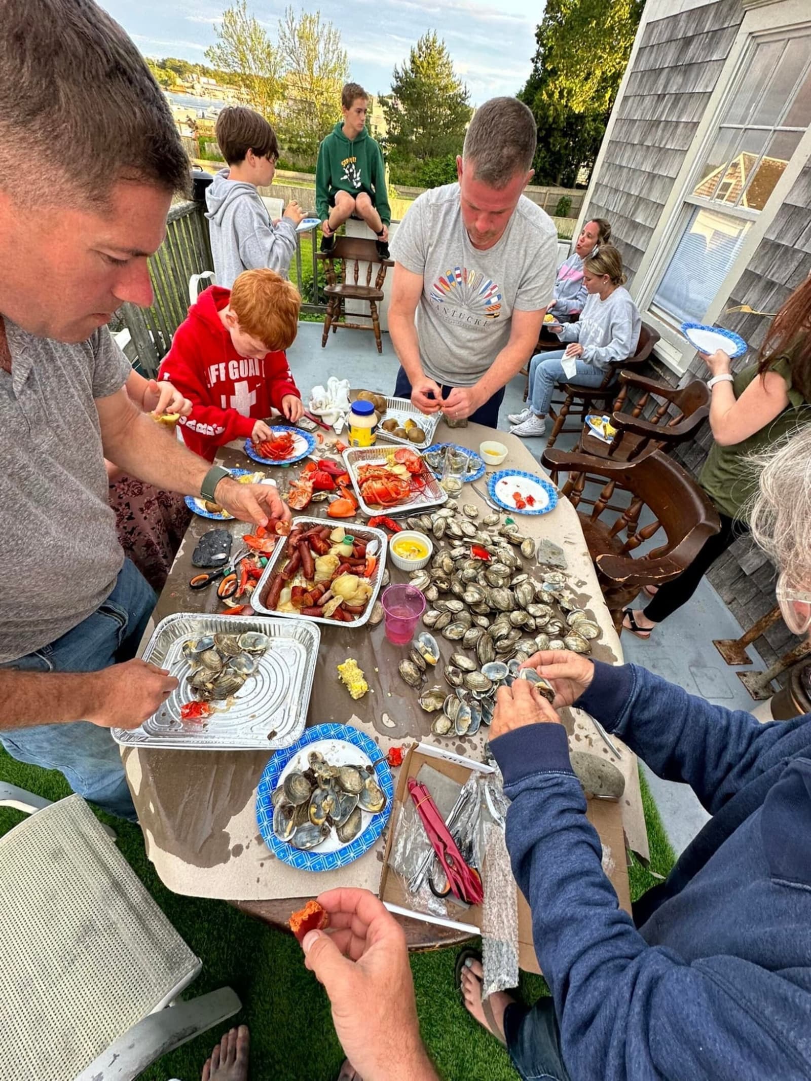 Family around the table on the porch, lobsters cracked open, steamers, corn, kids in the background