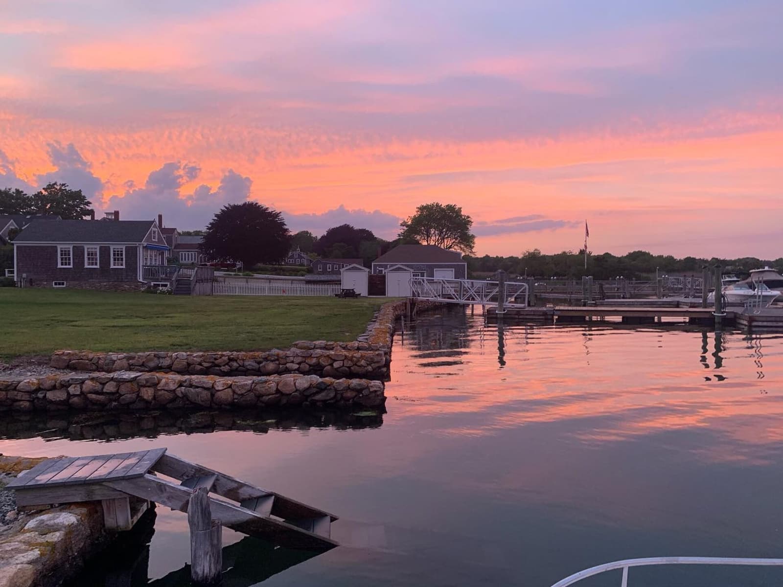 Pink sky reflecting on still water, stone seawall, docks, and shingled houses