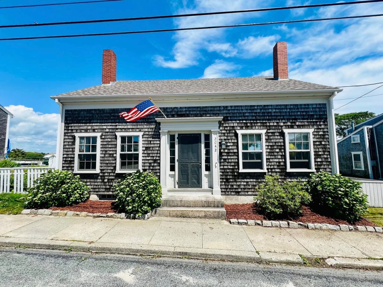 Full facade of 2042 Main Road, symmetrical with flag, dual chimneys, and 2042 address visible